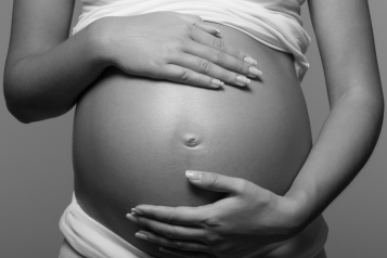 Black and white image of a pregnant person cradling their belly.