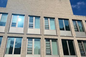 A modern, beige brick building with large windows reflecting the blue sky. The word "HEALTH" is displayed in large white capital letters on the top.